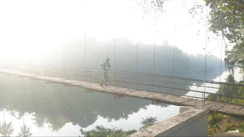 A runner crosses a suspension bridge over the Sangker River